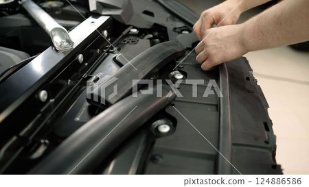 Car underhold repair, close-up. Specialist works on detailing an expensive car. Rubber under the hood, car repair. 124886586