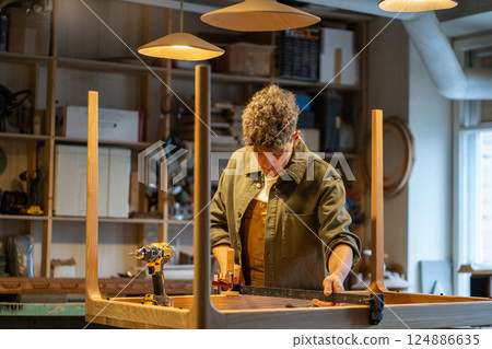Carpenter uses clamp to secure wooden table base for smooth installation in workshop. Custom design 124886635