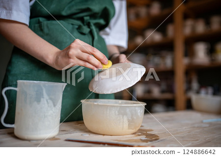 Coating ceramic tableware with glaze for durability. Potter hands using sponge for processing plate 124886642