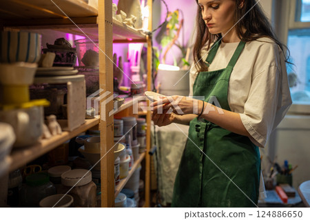 Female stacking ready clay products on pottery workshop shelves for drying. Store handmade dishes Female stacking ready clay products on pottery workshop shelves for drying. Store handmade dishes 124886650