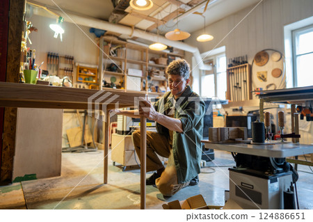 Woodworker reviews table assembly, satisfied with outcome in carpentry workshop. Furniture design Woodworker reviews table assembly, satisfied with outcome in carpentry workshop. Furniture design 124886651