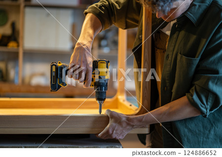 Woodworker secures table base to tabletop with power drill in carpentry studio. Accurate measurement 124886652