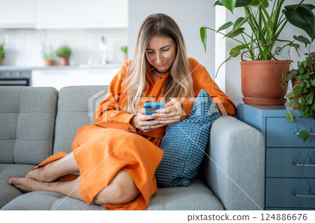 Positive woman resting on couch at home, absorbed in smartphone, enjoying time. Web feed connection Positive woman resting on couch at home, absorbed in smartphone, enjoying time. Web feed connection 124886676