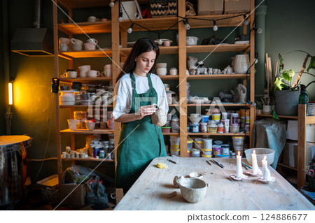 Female potter hold and attach handle to clay mug for material bonding, preparing for drying, firing Female potter hold and attach handle to clay mug for material bonding, preparing for drying, firing 124886677