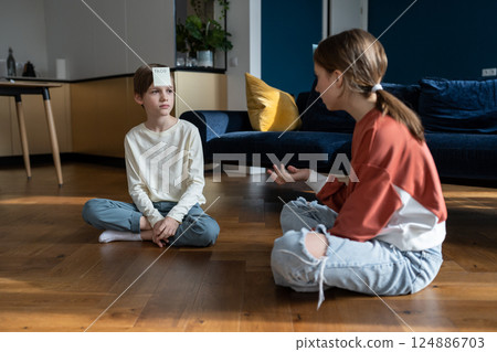 Small children boy and girl playing guessing game with sticky notes while sitting on floor at home Small children boy and girl playing guessing game with sticky notes while sitting on floor at home 124886703