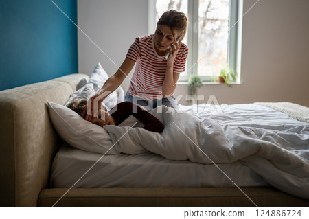Worried young woman mother calling to pediatrician while measuring son temperature at home Worried young woman mother calling to pediatrician while measuring son temperature at home 124886724