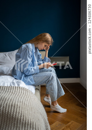 Worried young woman looking at smartphone screen feel nervous about posting on social media Worried young woman looking at smartphone screen feel nervous about posting on social media 124886730