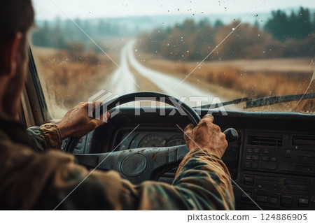 Man drives truck on moody rural road POV, hands grip wheel firmly navigating wet track, overcast sky enhances solitary moody journey feel, great atmospheric moody travel stock visual. 124886905