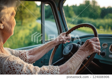 Senior woman drives classic car along sunlit country road POV, wrinkled hands firmly grip large steering wheel, timeless scene shows active senior lifestyle, beautiful senior independence. 124886906