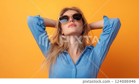 A blonde woman wearing a blue checkered shirt and sunglasses, stretching her arms back 124886946