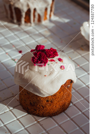 Orthodox Easter cake with raisins. Kulich topped with a sweet white glaze, dried roses and colorful sprinkles on a white countertop Orthodox Easter cake with raisins. Kulich topped with a sweet white glaze, dried roses and colorful sprinkles on a white countertop 124887780