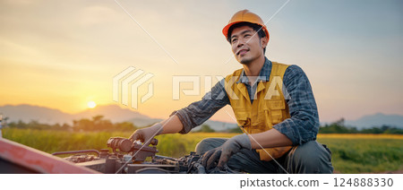 Worker performing maintenance on machinery at sunset in field 124888330