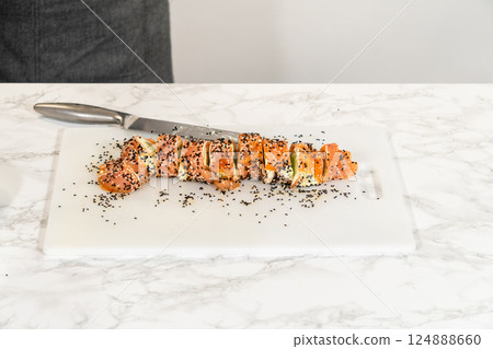 A sharp knife is used to slice the sesame-coated smoked salmon roll into uniform pieces, ready to be served as appetizers. 124888660