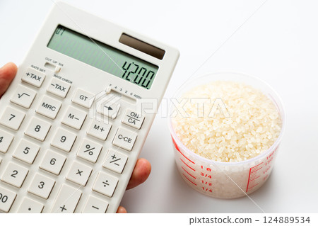 手拿著量杯的米和一個計算器 124889534