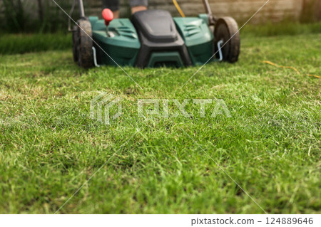 Gardening work tools. Green electric aerator scarifier for soil cultivation and compaction on bright lush green lawn grass. Professional lawn care service. Grass maintenance. Place for text. 124889646
