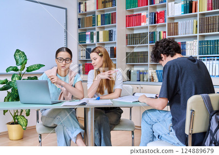 Group of students teenagers sitting together at desk in library preparing for tests exams Group of students teenagers sitting together at desk in library preparing for tests exams 124889679