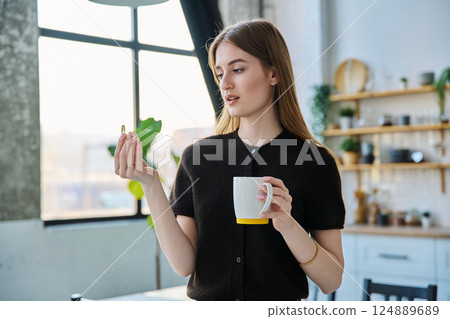 Young beautiful woman taking capsule with fish oil Omega 3, at home 124889689