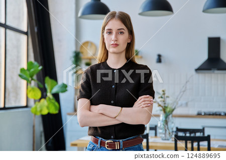 Portrait of serious female teenager looking at camera with crossed arms in home 124889695