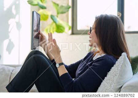 Portrait of middle aged woman using digital tablet sitting on sofa at home 124889702