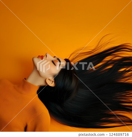 Woman with long black hair is laying on an orange background. She has red lipstick on her lips 124889716
