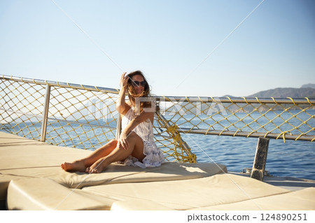 Smiling woman in summer dress relaxing on yacht deck under bright morning sun 124890251