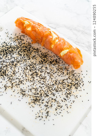 Smoked salmon roll rolled over a mixture of black and white sesame seeds, creating a flavorful and textured coating. 124890255
