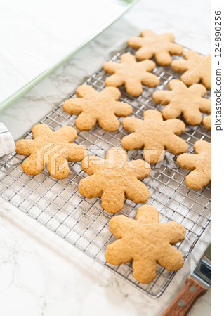 Angled top view of amber gingerbread cookies in snowflake shapes cooling on a wire rack, showcasing their golden-brown texture and festive design. 124890256