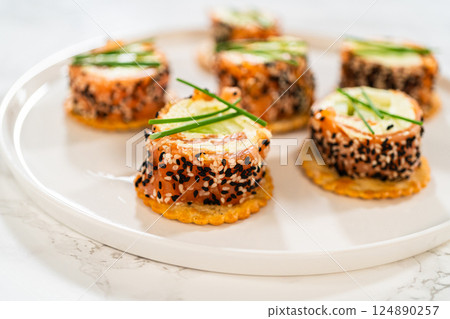 A beautifully plated presentation of smoked salmon jumbo cream cheese rolls on a round white plate. Each roll is sliced to reveal the creamy filling, accented by cucumber slices and wrapped in smoked A beautifully plated presentation of smoked salmon jumbo cream cheese rolls on a round white plate. Each roll is sliced to reveal the creamy filling, accented by cucumber slices and wrapped in smoked 124890257