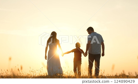 Family holding hands in field at sunset. Father dad kid boy child mother mom on golden rays sun go forward symbolizing hope bright future happy cheery memories time together. Strong family ties bonds 124890429