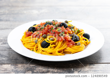 Italian Pasta puttanesca with tomato sauce, capers, and black olives on wooden table 124890549