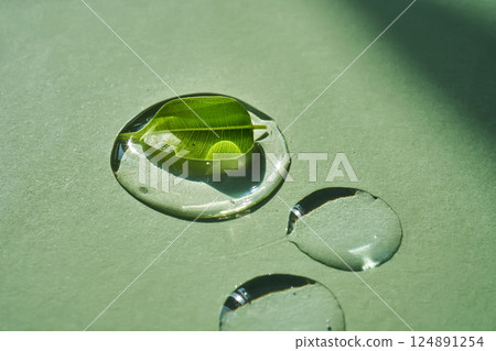 Drop of face serum with green leaf on green background. Drop of face serum with green leaf on green background. 124891254