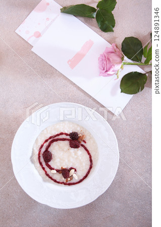 Homemade rice porridge for breakfast. Porridge with blackberries. View from above. Healthy eating. Top view. Pink roses on the table. 124891346