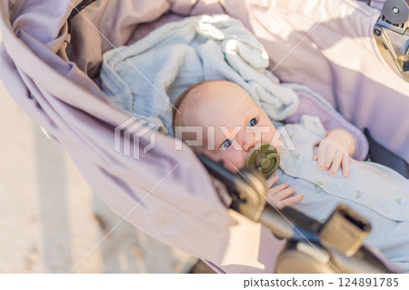 Mother walking with her baby in a stroller in the park. Peaceful outdoor bonding time. Parenthood, baby care, and family lifestyle concept Mother walking with her baby in a stroller in the park. Peaceful outdoor bonding time. Parenthood, baby care, and family lifestyle concept 124891785