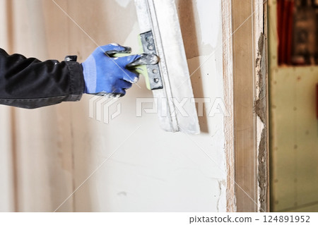 Close-up of a smooth plastered wall. Hands with a metal spatula. Apartment renovation. Leveling the plastered wall. With space to copy. High quality photo 124891952