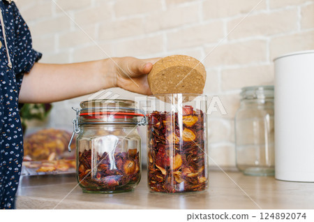 Woman Organizes Dried Fruit in Glass Jars on Kitchen Countertop Woman Organizes Dried Fruit in Glass Jars on Kitchen Countertop 124892074