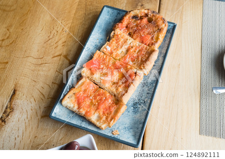 Traditional spanish pan con tomate on blue plate with olive garnish Traditional spanish pan con tomate on blue plate with olive garnish 124892111