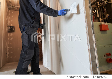 A construction plasterer levels a layer of plaster on a wall using a repair and construction spatula with one hand, holding the rule with the other. Leaving room for copying. High quality photo 124892820