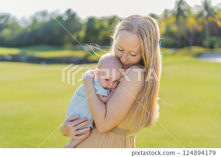 Mother and newborn baby on a meadow in the park. Tender bonding moment in nature. Parenthood, love, and family connection concept 124894179