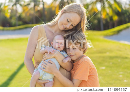 Mother, older son, and newborn baby on a meadow in the park. Family spending quality time together in nature. Parenthood, love, and family bond concept Mother, older son, and newborn baby on a meadow in the park. Family spending quality time together in nature. Parenthood, love, and family bond concept 124894367