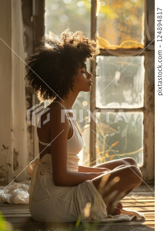 Peaceful Young Woman Meditating by Sunny Window in Cozy Wooden Room 124894817