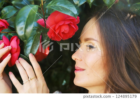 Woman admiring red camellia flowers up close 124895179