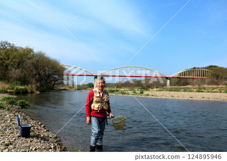 A fisherman wearing waders and catching river insects with a dip net A fisherman wearing waders and catching river insects with a dip net 124895946