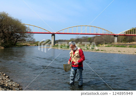 A fisherman wearing waders and catching river insects with a dip net A fisherman wearing waders and catching river insects with a dip net 124895949