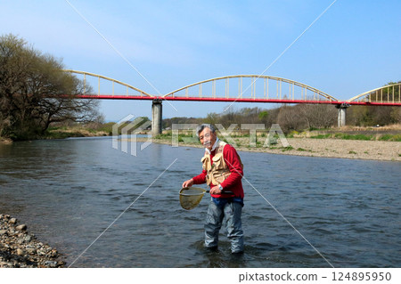 A fisherman wearing waders and catching river insects with a dip net A fisherman wearing waders and catching river insects with a dip net 124895950