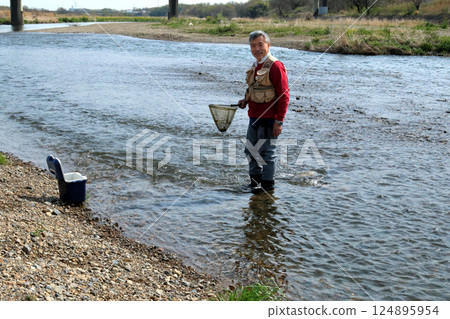 A fisherman wearing waders and catching river insects with a dip net A fisherman wearing waders and catching river insects with a dip net 124895954