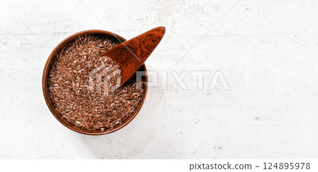 Small wooden bowl full of common flax linseed - Linum usitatissimum - little scoop inside, on white stone like desk, view from above, space for text right side 124895978
