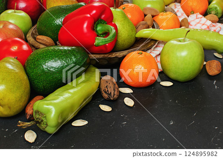 Mixed fruits and vegetables - red peppers, avocado, apples, pears, tangerines, pecan nuts, almonds and pumpkin seeds on wooden bowl, close up view Mixed fruits and vegetables - red peppers, avocado, apples, pears, tangerines, pecan nuts, almonds and pumpkin seeds on wooden bowl, close up view 124895982