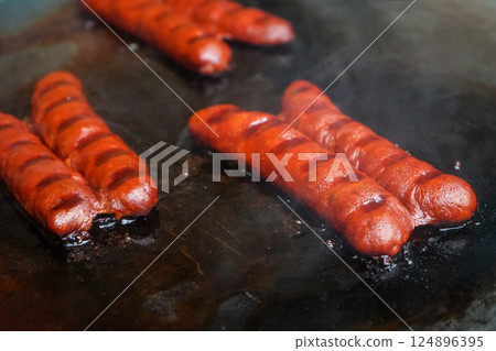 Small bratwurst / hot dog frankfurter sausages grilled on electric grill, smoke visible above 124896395