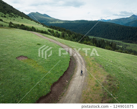 Aerial view of woman riding mountain bike on flowering grassland mountain Aerial view of woman riding mountain bike on flowering grassland mountain 124901075