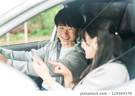 一對年輕的亞洲夫婦在車上一邊看智慧型手機一邊聊天,丈夫和妻子 一對年輕的亞洲夫婦在車上一邊看智慧型手機一邊聊天,丈夫和妻子 124904376